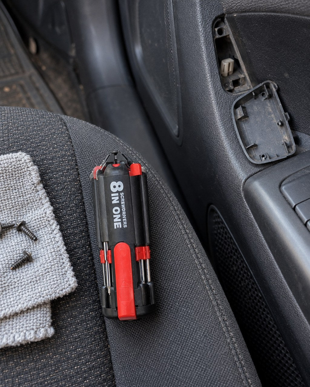 Destornillador 8 en 1 sobre el asiento de un auto junto a un panel de puerta desarmado